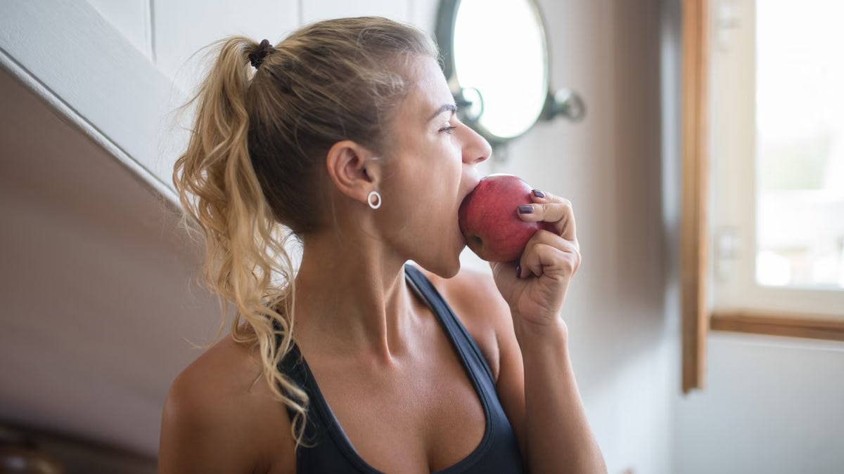 Young woman in a tank top eating an apple for a healthy snack indoors.